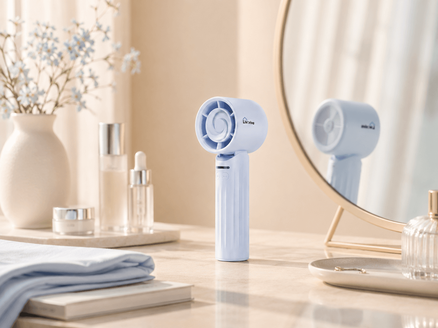 Light blue handheld fan on a vanity table with skincare products and a gold mirror.